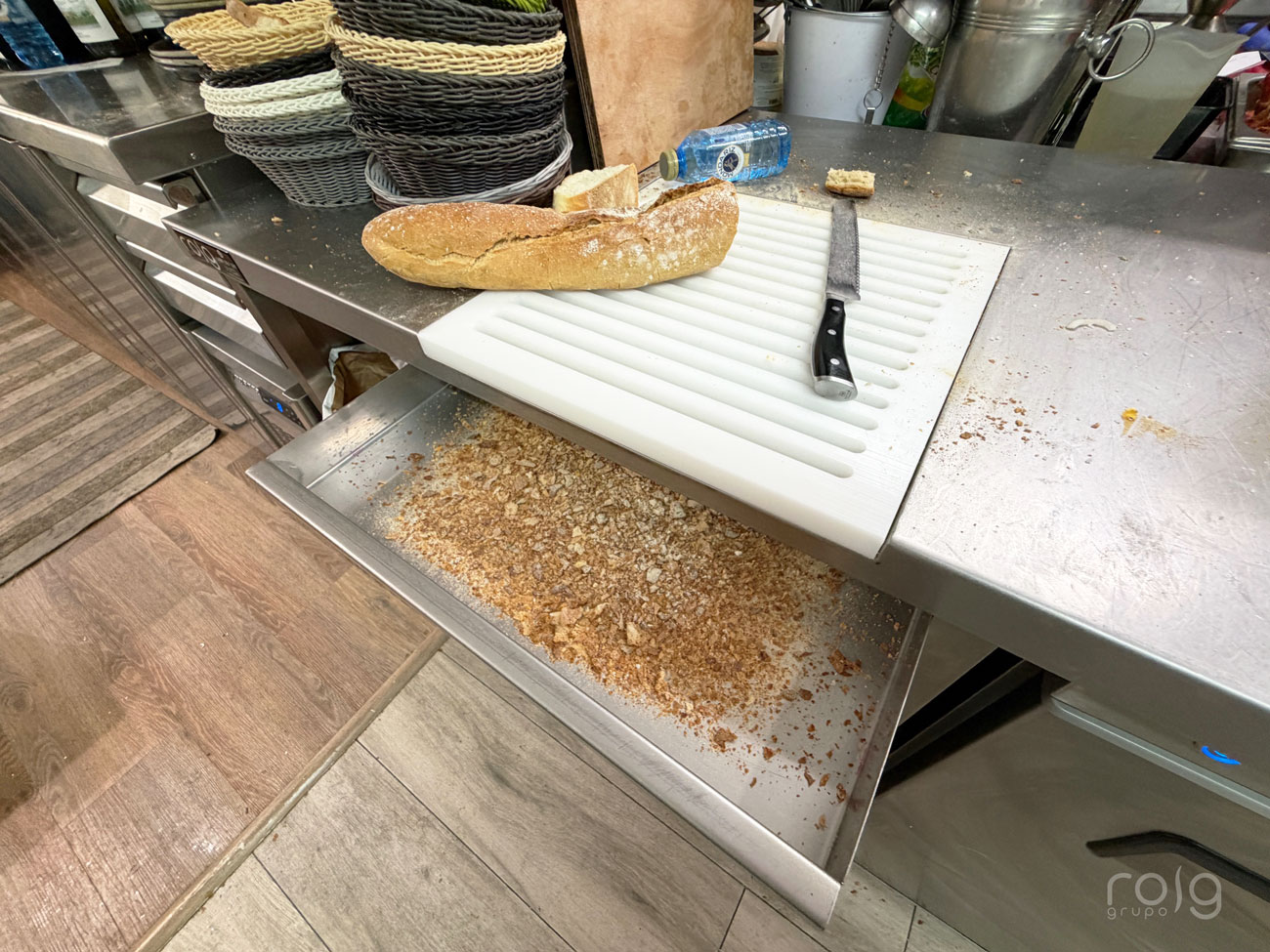 Detalle de la zona de corte de pan con tabla ranurada y cajón recogemigas en el mesado inox del Restaurante A Meca